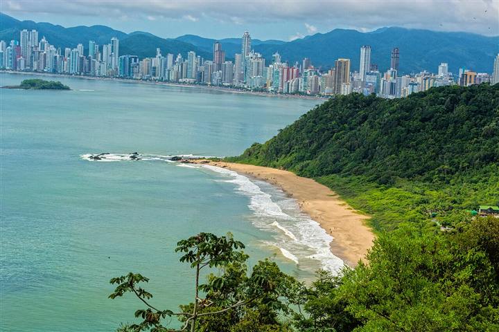 Vista aérea de Balneário Camboriú com morro verde, praia e prédios ao fundo
